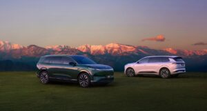 Two Dongfeng 008 SUVs, one dark green and one silver, parked on grass in front of mountains at dusk