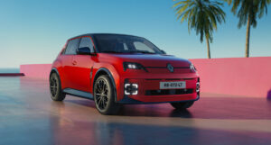 Red Renault 5 E-Tech electric hatchback, front three-quarter view, beside a pink wall and palm trees
