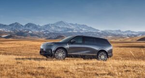 Un SUV XPENG GX gris à six places est garé de côté dans une prairie dorée, avec des montagnes enneigées en arrière-plan.